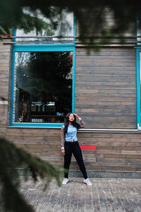 Hipster african american girl wearing jeans shirt with leopard sleeves posing at street against wooden house with windows.