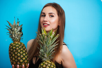 Portrait of young woman in swimsuit with pineapple on blue background. Summer season