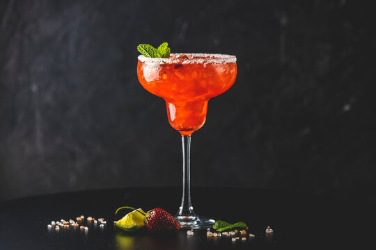Frozen strawberry lime mint margarita in tall footed glass on the dark background. Luxury alcohol fresh drink