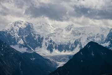 Awesome landscape with huge glacial mountains in bad cloudy weather. Low stormy clouds touch top of snowy mountain with glaciers. Storm is coming due to mountains. Gloomy overcast atmospheric scenery.