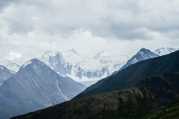 Fototapeta premium Wonderful view to huge glaciers on great snowy mountain range behind big rocks under gloomy cloudy sky. Pointy tops of giant rocky mountains. Awesome beauty of highlands. Atmospheric alpine landscape.