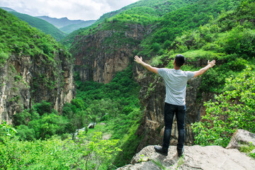 A man with open hands stands by a cliff