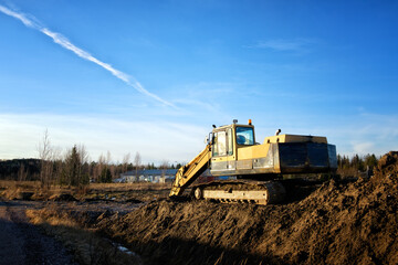 Yellow excavator on a road construction site against blue sky.