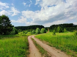 beautiful blue sky with clouds over a winding country road in a green hilly area