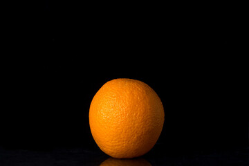 One orange on a black background. Tropical fruits. A whole orange in a peel.