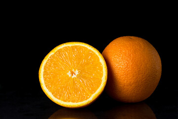 Oranges on a black background. One orange is cut in half, the other is whole. Tropical fruits.