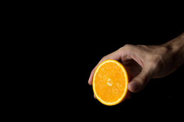 Hand holds an orange, an orange is cut in half. Photo on a black background.
