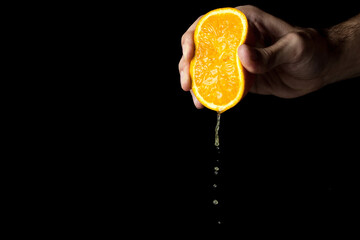 A hand squeezes an orange on a black background. The orange is cut in half.