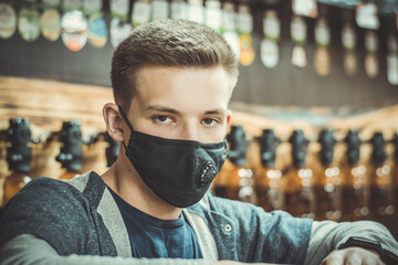 Young guy in a black protective mask. A large portrait of a young man in a medical mask. Pandemic. Coronavirus. Covid 19. Summer 2020. Beer seller awaiting buyers.