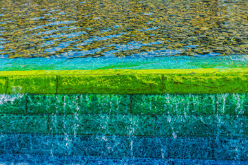 Bright fountain water on a green and blue wall with sun reflection background, Zabeel Park, Dubai, United Arab Emirates