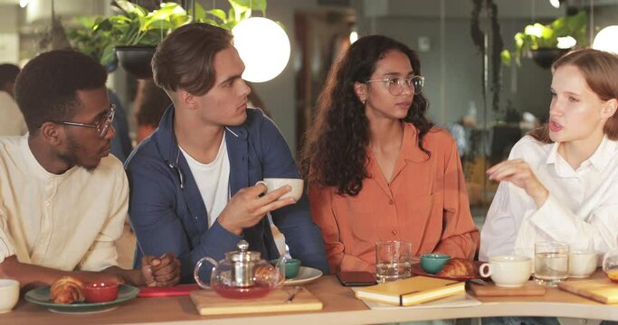 Millennial atractive girl talking while sharing thoughts with coworkers in modern cafe. Successful multiethnic young people listening female colleague. Concept of communication.