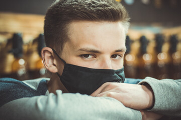 Young guy in a black protective mask. A large portrait of a young man in a medical mask. Pandemic. Coronavirus. Covid 19. Summer 2020. Beer seller awaiting buyers. Beer pub