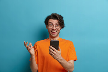 Technology and online communication concept. Happy unshaven man uses smartphone, gestures with...