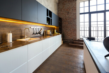 luxury studio apartment with a free layout in a loft style in dark colors. Stylish modern kitchen area with an island, cozy bedroom area with fireplace and personal gym