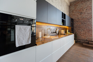 luxury studio apartment with a free layout in a loft style in dark colors. Stylish modern kitchen area with an island, cozy bedroom area with fireplace and personal gym
