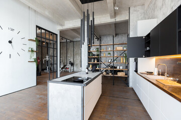 luxury studio apartment with a free layout in a loft style in dark colors. Stylish modern kitchen area with an island, cozy bedroom area with fireplace and personal gym