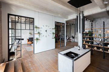 luxury studio apartment with a free layout in a loft style in dark colors. Stylish modern kitchen area with an island, cozy bedroom area with fireplace and personal gym