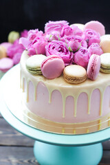 Elegant pink wedding cake decorated with melted white chocolate, beautiful fresh roses and macaroons. Black background.