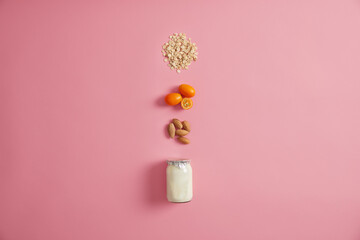 Layout of fresh yoghurt with nuts, cumquat and oat to prepare delicious oatmeal. Homemade breakfast with much vitamins and nutrients. Products for healthy snack on rosy background. Top view.