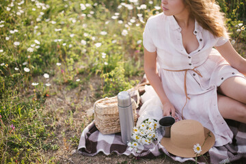 Young beautiful woman having picnic with tea in chamomile field.