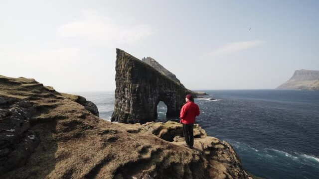 Man Standing in Rocky Cliffs Overviewing Large Rock in Faroe Islands