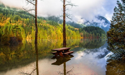 Fototapeta na wymiar Autumn flood, High level of water at picnic area near Buntzen Lake, early snowfalls and heavy rains, a lot of snow melted in the mountains, floods flooded the picnic place 