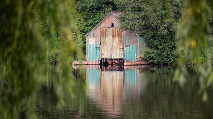 An old corrugated tin disused boathouse surrounded by trees standing at the edge of water and...