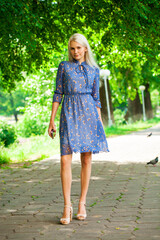 Portrait of a young blonde woman in blue dress walking in summer parkpark