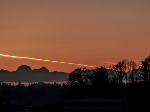 Bright contrail in the sky and silhouette of Cascade Range and forest in the foreground in the twilight hours of Mercer Island in Washington State.