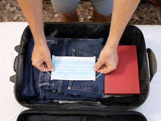 Summer vacations,new normal,hands of adult man wearing shorts preparing the luggage,clothes,medical mask in suitcase for safety,travel preparation on holidays,New normal life