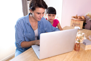 mother working at home, typing on computer, daughter watching what mom does