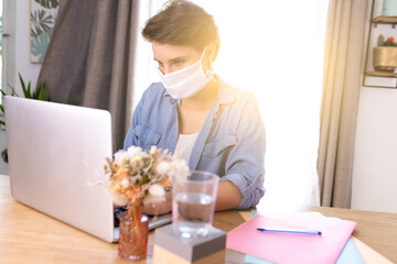 a woman wearing a surgical mask and teleworking at home