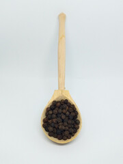 Closeup isolate: black pepper in a wooden spoon. A handful of pepper is measured with a spoon, lies on a white background.