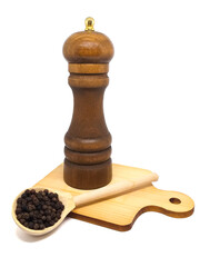 closeup isolate: mill for grinding black pepper and a handful of spices in a wooden spoon on a background of a wooden cutting board. A handful of pepper in a spoon near the mill on a white background
