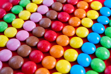 Close-up round colored dragee sweets are laid out in a rainbow pattern. Chocolate candies on a red background. Selective focus