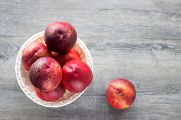 Fresh organic nectarines in a white basket on a gray wooden table.