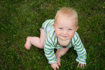 cute little baby sitting on the green grass and looking upwards, topview