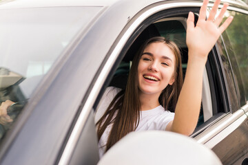 Hello. Beautiful young cheerful women looking at camera with smile and waving while sitting in her car