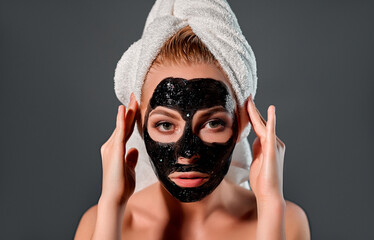 Beautiful woman with black peel-off mask on a gray background.