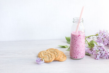 Berry smoothie in a glass jar with a straw for cocktails, cereal cookies, a branch of lilac, on a light background. Healthy lifestyle, diet, detox. Refusal of plastic. Daylight, selective focus.