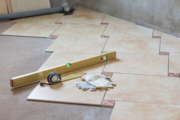 bathroom. It is being renovated. Ceramic tiles are laid on the floor. Focus is on level, tape measure and gloves. Close-up.