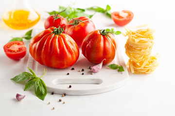 Assorted tomatoes with basil, garlic, spice and raw pasta for italian cuisine. Healthy food concept on white background.