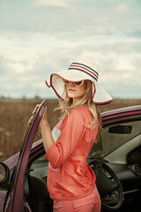 Portrait of young woman near car in sunglasses and hat. Driver. Girl in automobile, outdoors, summer
