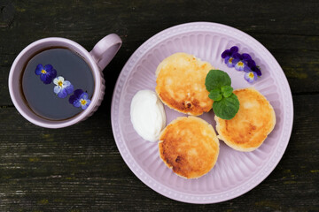 Cheesecakes with sour cream, decorated with flowers violets and mint and a cup of tea - a healthy breakfast.