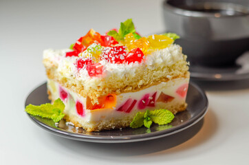 A portion of cream cake with pieces of colorful jelly and sprinkled with coconut flakes