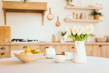 Fototapeta na wymiar bright wooden kitchen in the style of Provence and Scandinavia, on the table dishes, a set of fruit and a bouquet of flowers in a vase. tulips and apples. The concept of a women's holiday