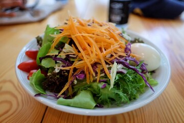 Fresh vegetables salad with boiled egg in a white plate on wooden dinning table 