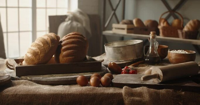 Fresh loafs of white bread in basket lying on table with eggs and table. Traditional components of bread recipe at bakery. Fresh loafs for breakfast - close up shot 4k footage