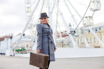 Young woman wearing hat walking outdoors on the city street near ferris wheel smiling cheerful.