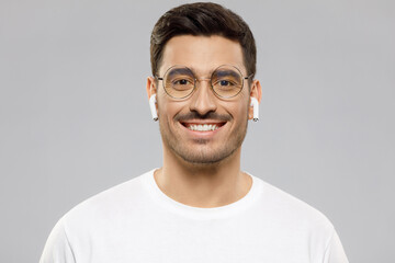 Close-up portrait of young handsome smiling man wearing white t-shirt and wireless earphones,...